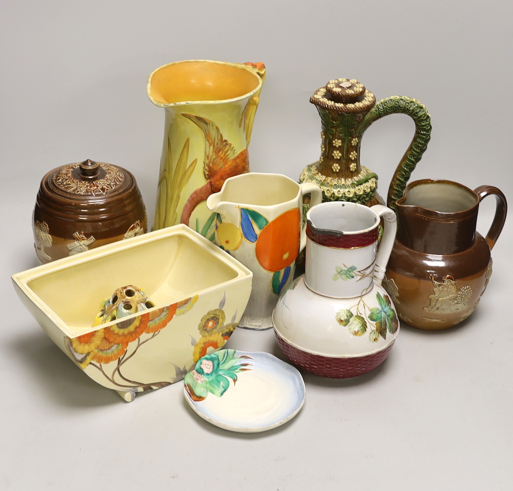 Four Clarice Cliff items; a miniature dish, jug, etc. together with four jugs and a biscuit barrel, tallest jug 24cm